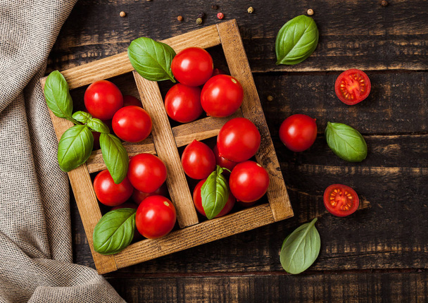 Organic Tomatoes with basil and linen towel in vintage wooden box on wooden kitchen table - Valokuva, kuva