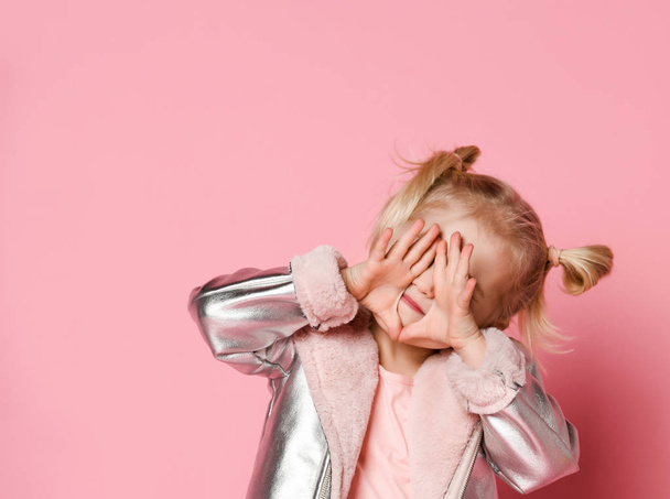 Portrait of a little girl in stylish clothing sitting on pink background and playing up - Foto, afbeelding