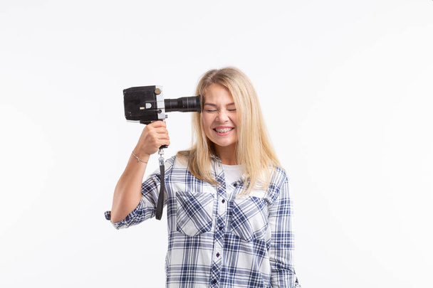Witz, Foto und Gestenkonzept - junge lustige dumme Frau posiert mit Kamera in der Nähe seines Kopfes auf weißem Hintergrund - Foto, Bild