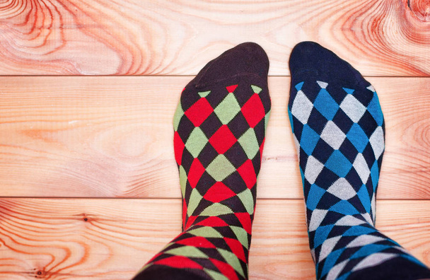 zwei Beine in verschiedenen kunterbunten Socken auf einem Holzboden - Foto, Bild