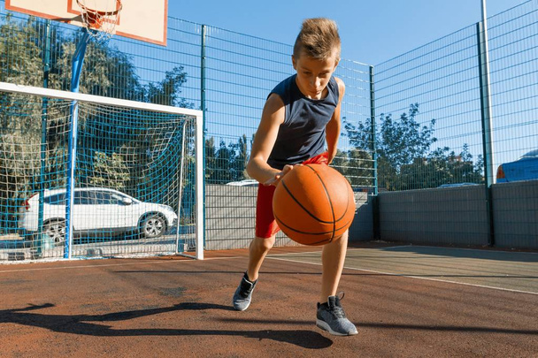Caucasian teenager boy street basketball player with ball on outdoor city basketball court - Foto, Imagen
