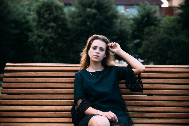 young brunette woman in black dress posing on bench - Foto, Bild