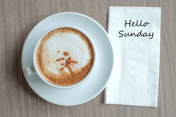 Текст Hello Sunday на бумаге с чашкой горячего кофе капучино на вкладке
 - Фото, изображение