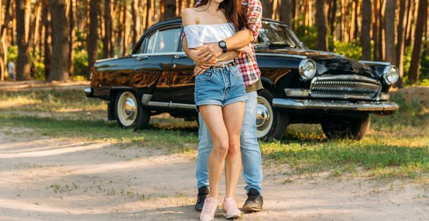 torso of a man and a woman holding hands, with a flower and with a clock on his hand. standing near the car. - Фото, изображение