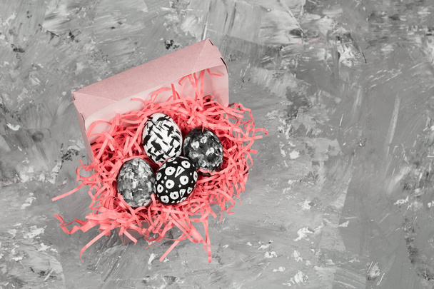 top view dyed eggs with black and white geometric pattern in a decorative pink nest on a concrete background - Фото, зображення