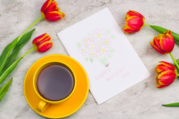 beautiful tulips ,cup of drink and handmade card with kid's drawing  for Mother's Day on marble background, top view - 写真・画像