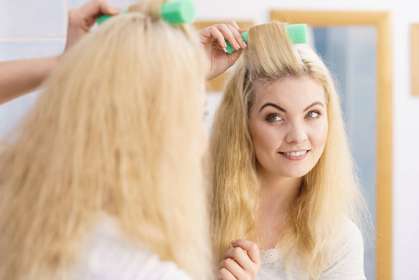 Blonde woman using hair rollers - Foto, afbeelding