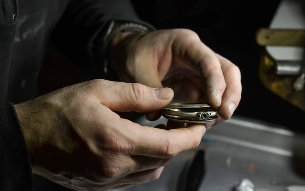The watchmaker holds the silver case of a vintage pocket watch in his workshop - Foto, Bild
