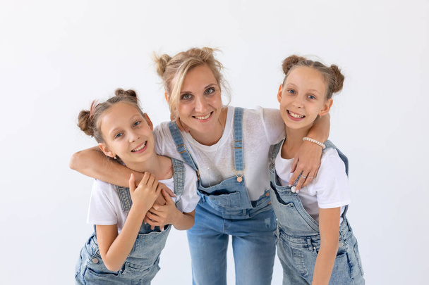 concepto de personas, familia e hijos - retrato de una madre encantadora abrazando a sus hijas gemelas sobre fondo blanco
 - Foto, imagen