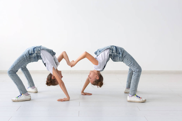 Családi és sportnapok koncepció - két acrobat iker lányok állva a kéz felett fehér háttér - Fotó, kép
