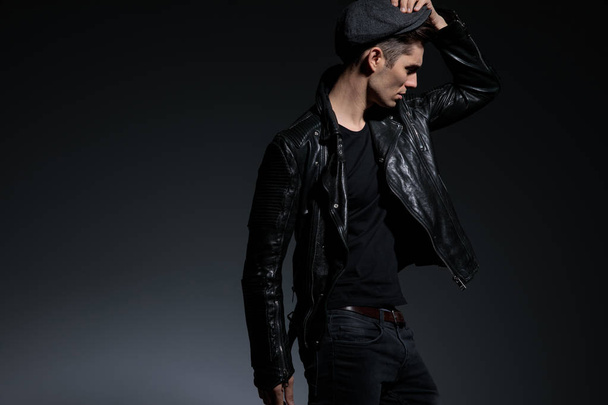 fashion man in leather jacket holding cap looks to side - Fotoğraf, Görsel