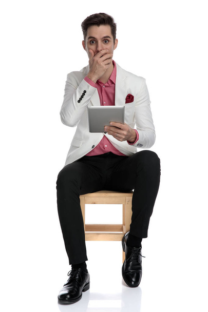młody biznesmen czytanie niesamowite wiadomości na swoim tablecie w pozycji siedzącej - Zdjęcie, obraz