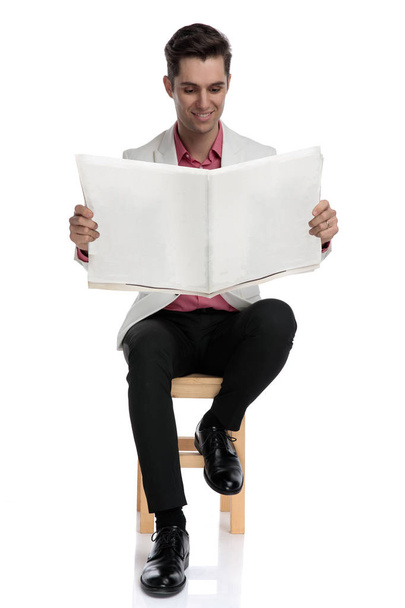 young stylish man sitting on chair and reads newspaper  - Фото, изображение