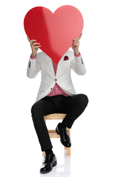 κάθεται ο σύγχρονος άνθρωπος, κρατώντας μια μεγάλη κόκκινη καρδιά πάνω στο πρόσωπό - Φωτογραφία, εικόνα
