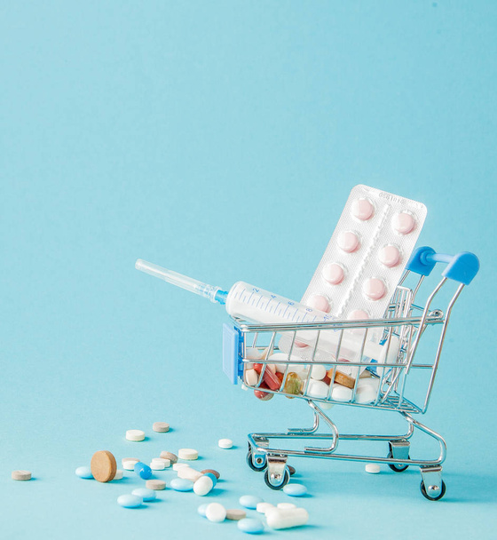 Pills and medical injection in shopping trolley on blue background. Creative idea for health care cost, drugstore, health insurance and pharmaceutical company business concept. Copy space - Photo, Image