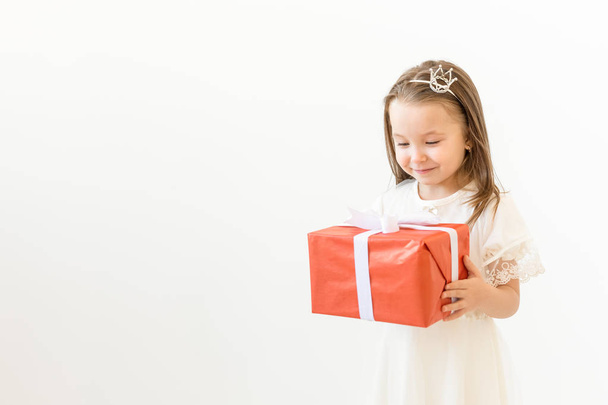 Vakantie en presenteert concept - kleine meisje glimlach en bedrijf rode geschenkdoos op witte achtergrond met kopie ruimte - Foto, afbeelding
