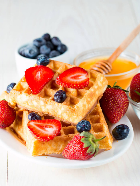 Photo of fresh homemade food made of berry Belgian waffles with honey, chocolate, strawberry, blueberry, maple syrup and cream. Healthy dessert breakfast concept with juice.  - Fotografie, Obrázek