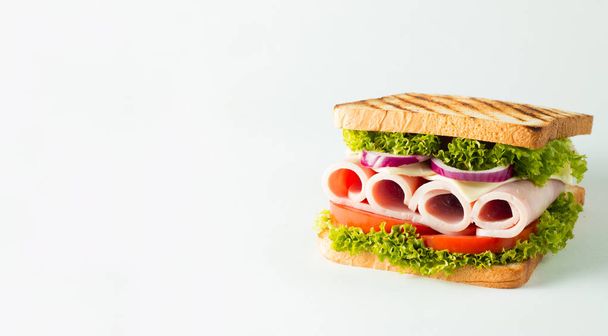 Close-up photo of a club sandwich. Sandwich with meat, prosciutto, salami, salad, vegetables, lettuce, tomato, onion and mustard on a fresh sliced rye bread on wooden background. Olives background. - Фото, изображение