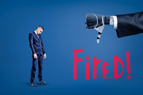 Sad businessman looking down and big close-up of robots hand doing thumbs down with title Fired below. - 写真・画像