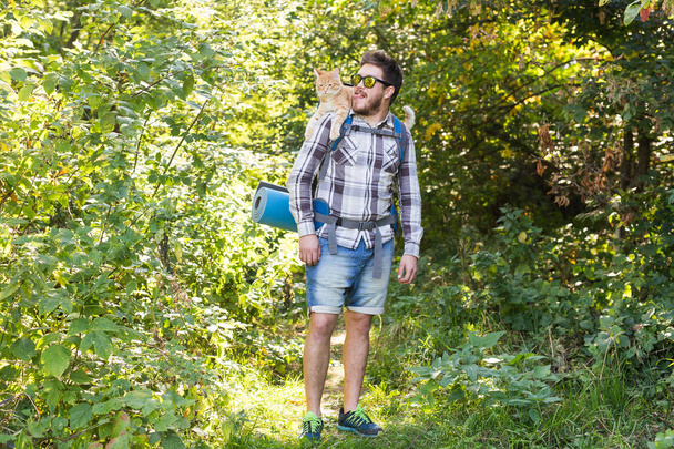Hike, tourism and nature concept - Young traveler with backpack and with his cat standing over forest background - Photo, Image