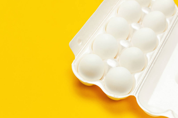 White chicken eggs in white packaging on yellow background top view flat lay copy space. Eggs in box, natural healthy food and organic farming concept. Creative food minimalistic background, Easter - Foto, imagen
