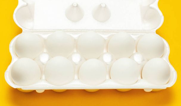 黄色の背景の上に白いパッケージに白い鶏の卵は、フラット レイアウト コピーの領域を表示します。ボックス、自然健康食品、有機農法の概念の卵。創作料理ミニマルな背景、イースター - 写真・画像