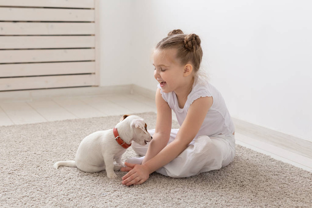 Gente, mascotas y concepto animal - Niña sentada en el suelo sobre fondo blanco y sosteniendo al cachorro Jack Russell Terrier
 - Foto, Imagen