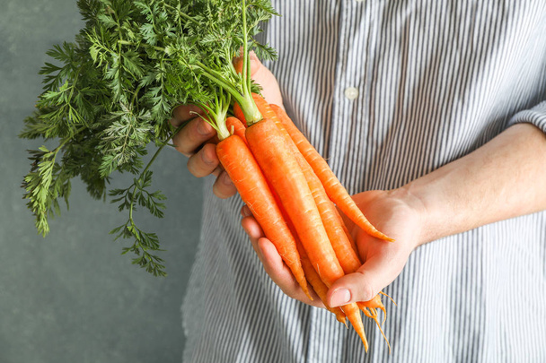 Фермер держит спелую морковку с верхушками в руках.
 - Фото, изображение