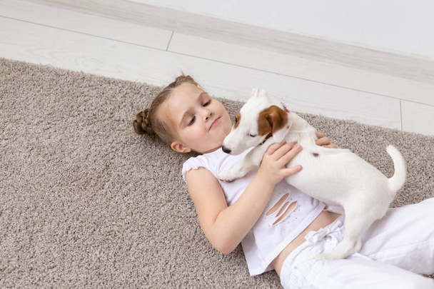 Pet, concept d'enfance et d'animal - Portrait d'une petite fille couchée sur le sol avec le chiot Jack Russell Terrier
 - Photo, image