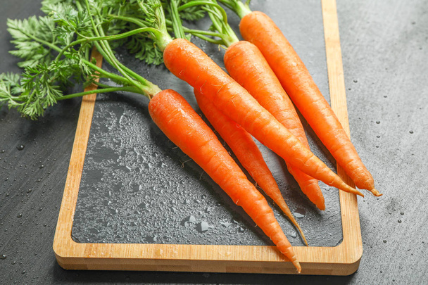 Planche à découper avec carottes mûres sur table noire, vue de dessus
 - Photo, image