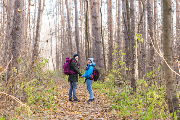 冒険旅行、観光、ハイキング、人々 の概念 - 秋の自然な背景の上にバックパックと歩いて笑顔のカップル - 写真・画像