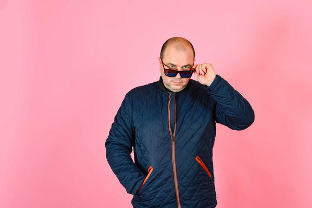 A man in a blue jacket and sunglasses on a pink background in the studio - Foto, imagen
