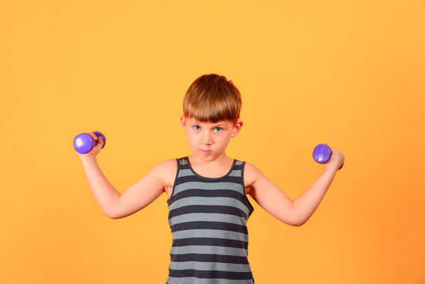 Een jongen met paarse halters gaat voor sport en lichamelijke oefeningen in de studio op een gele achtergrond doet - Foto, afbeelding