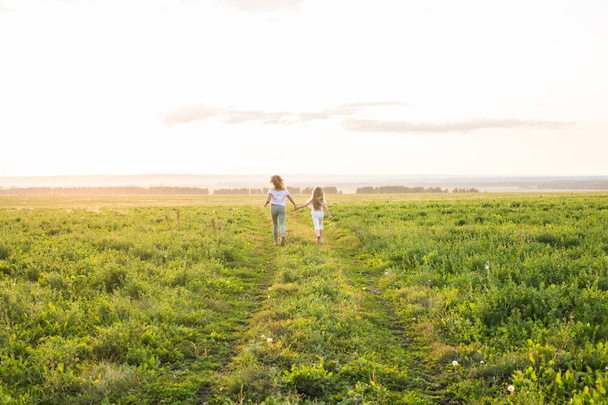 Семья, лето и праздник - мать, держащая дочерей за руку, бегает по зеленому полю
 - Фото, изображение
