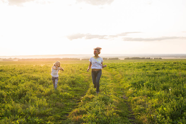 Family, summer and holiday concept - little daughter and mother run in the summer field - Фото, зображення