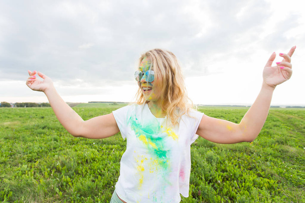 Fun, holi festival and holidays concept - Funny woman covered with color powder smiling over nature background - Foto, Imagem
