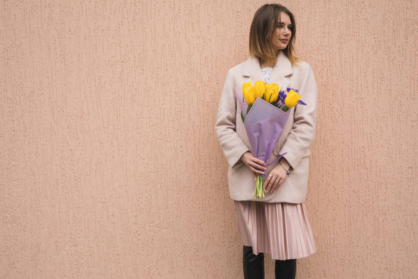 Woman holding a bouquet of yellow tulips at beige wall - Foto, afbeelding