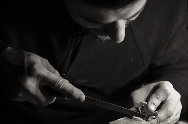 Mistr zlatník ve svých rukou drží pracovní nástroj a dělá na jeho pracovišti v dílně šperky šperky. - Fotografie, Obrázek