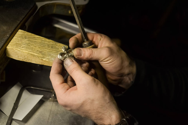 O mestre joalheiro segura a ferramenta de trabalho em suas mãos e faz jóias em seu local de trabalho na oficina de jóias
. - Foto, Imagem