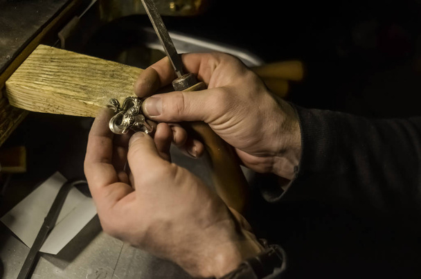De meester juwelier houdt het werktuig in zijn handen en maakt sieraden op zijn werkplek in de sieraden workshop. - Foto, afbeelding