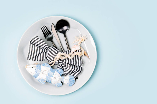 Tableware and sea decorations for serving a festive table. Plates, wine glasses and cutlery on blue background. Summer concept. Flat lay, top view - Photo, Image