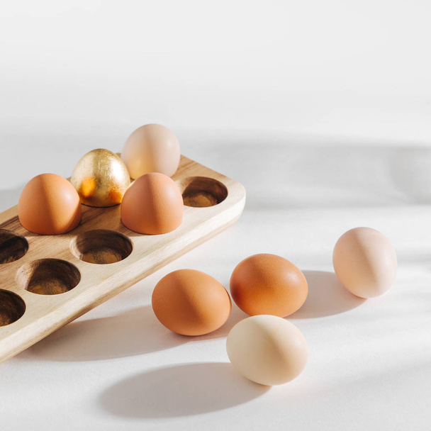 Яйца натурального цвета в деревянной яйцеклетке с солнечными огоньками. Произведения в пастельных тонах. Пасхальная концепция
.  - Фото, изображение
