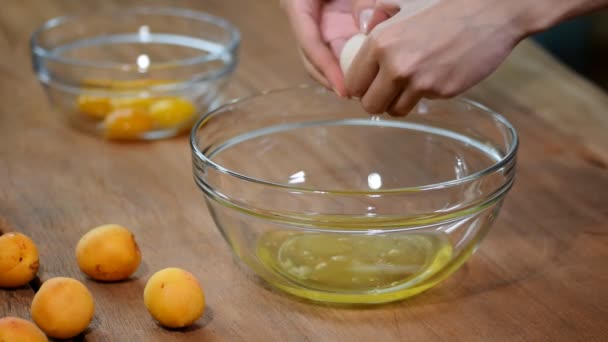 Manos de mujer rompiendo un huevo para separar clara de huevo y yemas
 - Metraje, vídeo