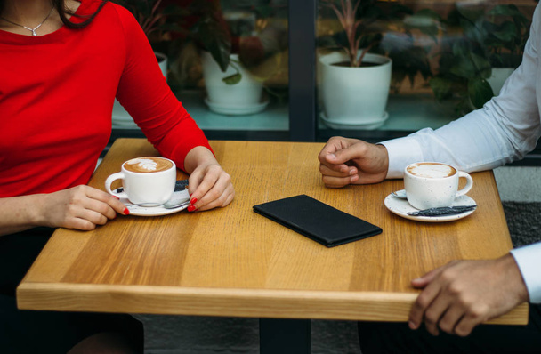ένα ζευγάρι, δύο, ένα άντρα και ένα κορίτσι κάθονται σε ένα καφενείο, πίνοντας καφέ, δύο κύπελλα καπουτσίνο στο τραπέζι, νομοσχέδιο για ένα ποτό. συζήτηση - Φωτογραφία, εικόνα