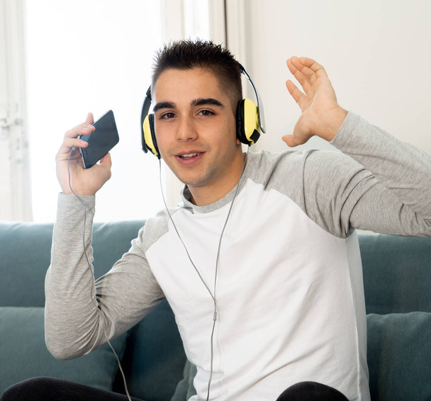 Portrait of young happy teenager male listening to music in headphones singing and dancing on sofa at home. In positive emotions, youth and happiness,Leisure Music and technology concept. - Photo, image