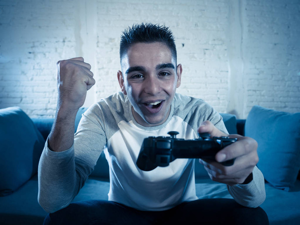 Portrait of young man having fun playing video games using wireless remote joystick with freak intense happy face celebrating winning. In Male game addiction to console play station and video. - Photo, image