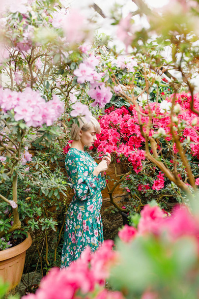 portrait of a young beautiful blonde woman in a green dress in a beautiful botanic garden with flowers - Foto, Imagen
