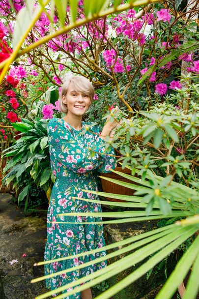 portrait of a young beautiful blonde woman in a green dress in a beautiful botanic garden with flowers - Foto, Bild