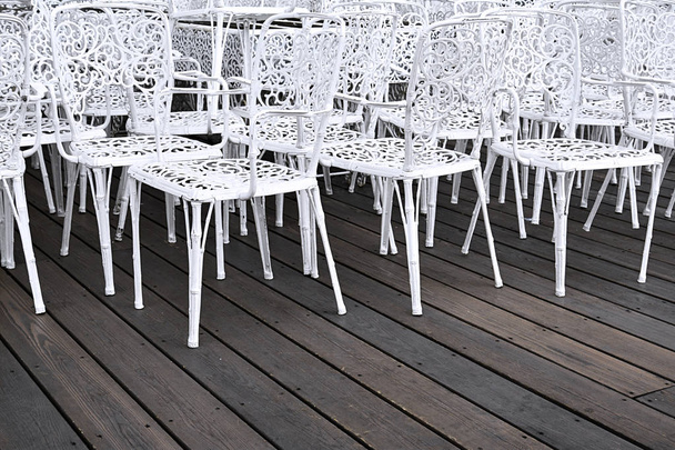 View of white openwork metal chairs standing on a brown floor. - Fotografie, Obrázek