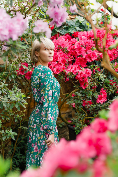 portrait of a young beautiful blonde woman in a green dress in a beautiful botanic garden with flowers - Foto, afbeelding